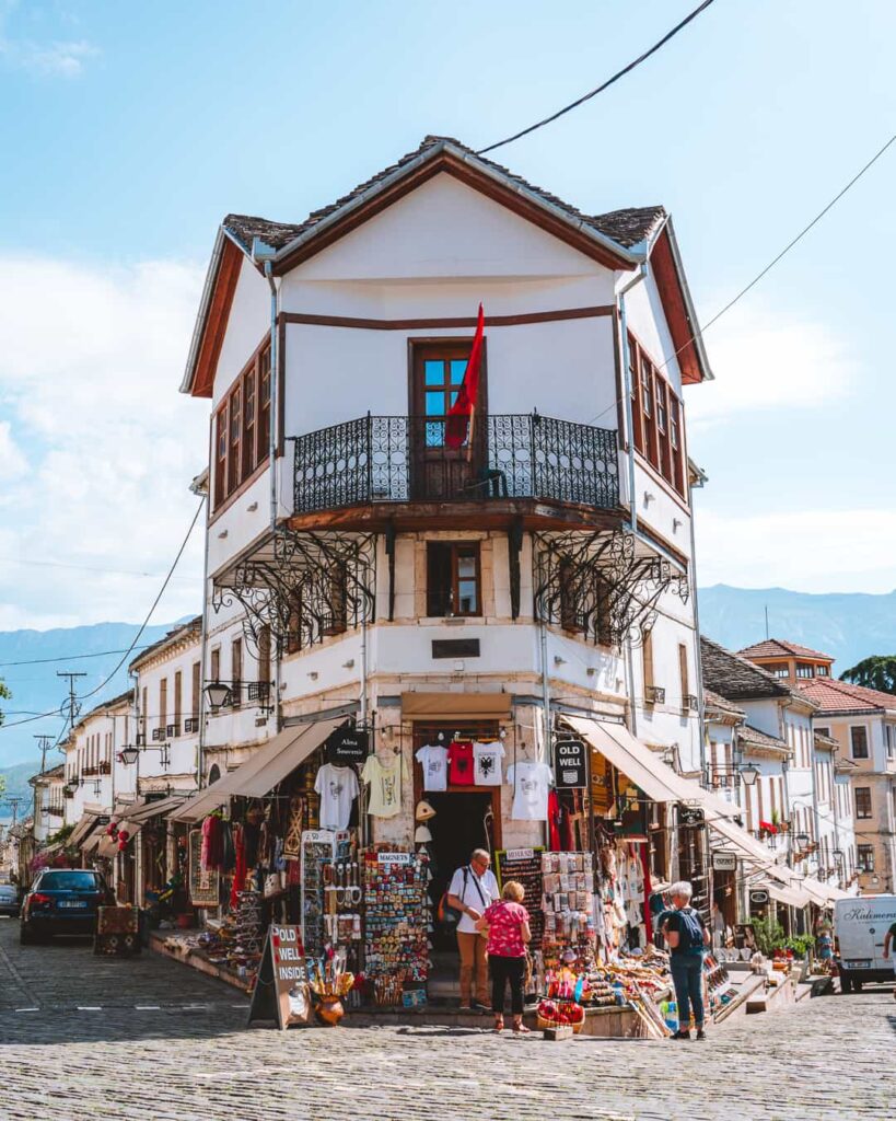 A traditional stone-and-timber Ottoman house flying the Albanian flag on a cobbled street in Gjirokastër, southern Albania.