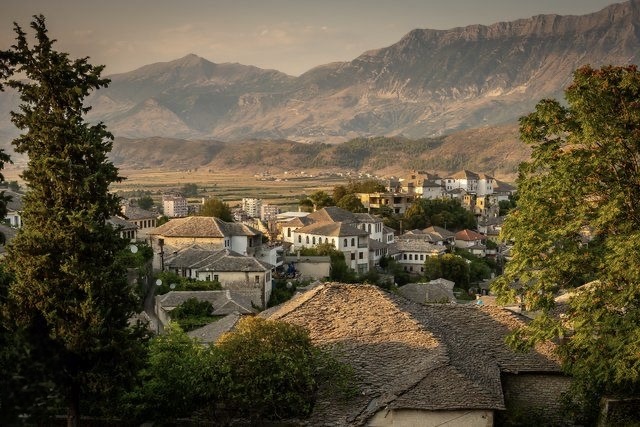 A historic Albanian stone town on a hilltop beneath rugged mountain peaks.
